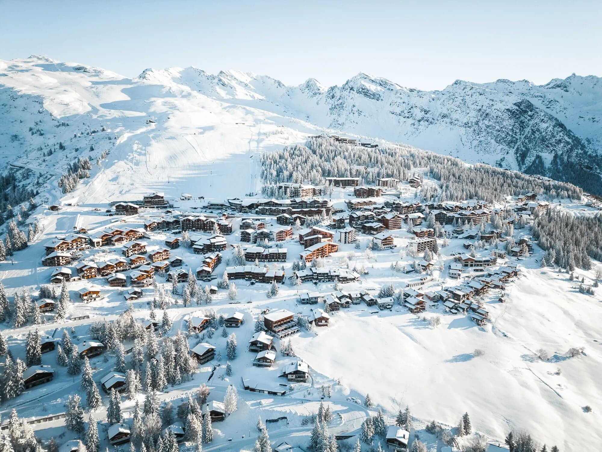 An aerial view of La Rosière's snow-covered chalets among frosted trees, with mountains behind.