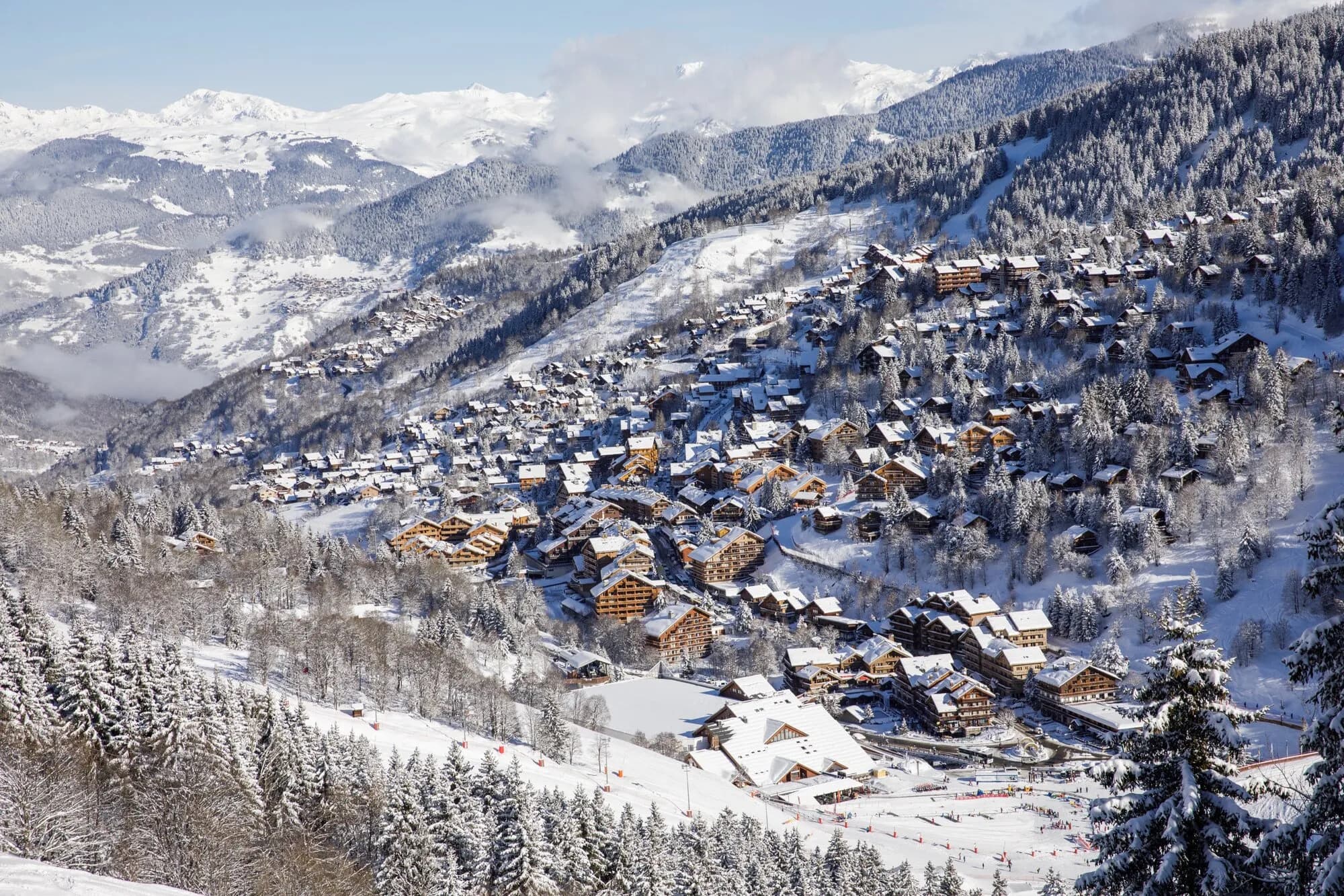 Chalets of Méribel-Centre spread across a snowy, forested hillside, with mountains beyond.
