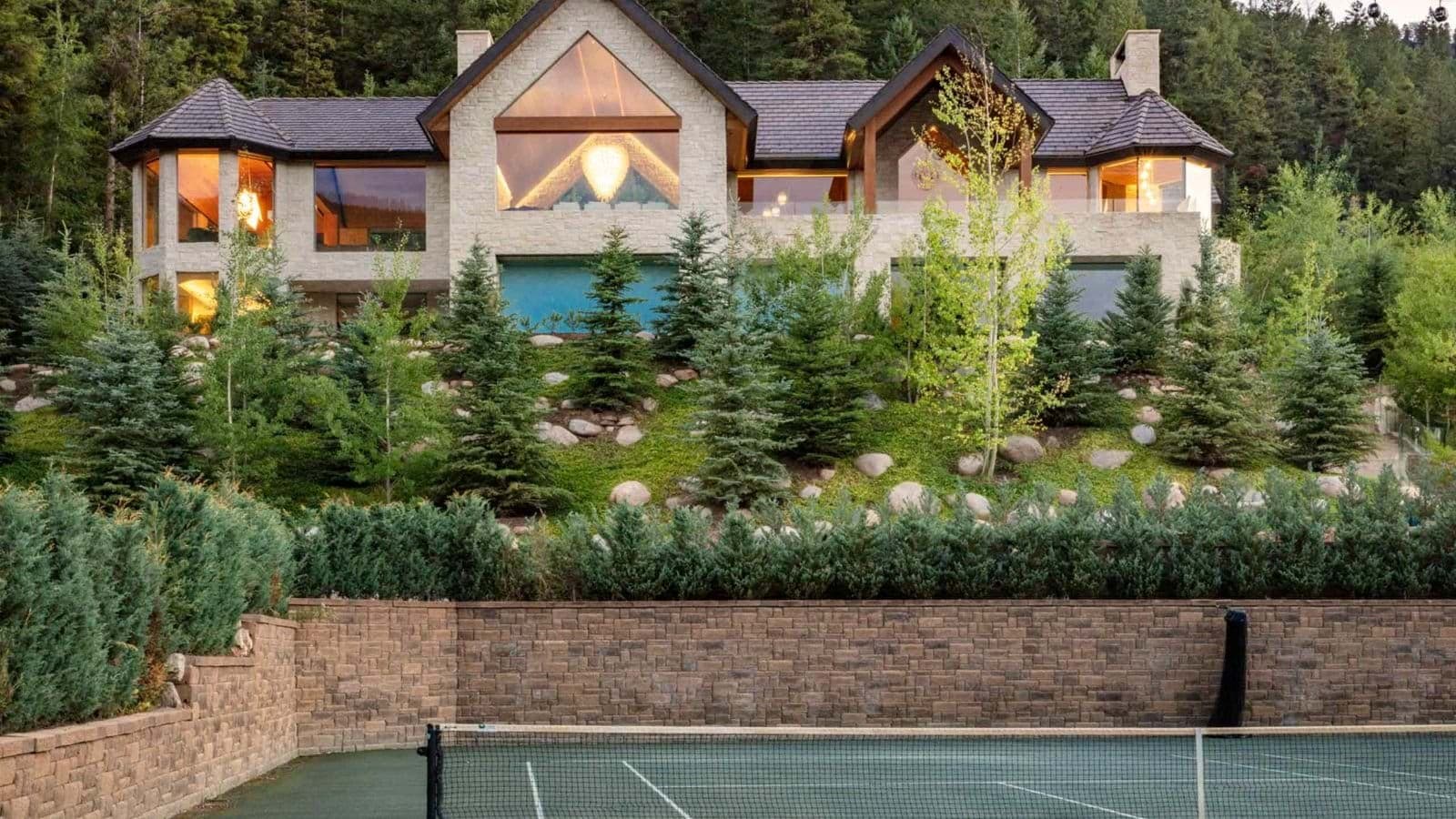 Private tennis court with forest backdrop and tiered stone landscaping