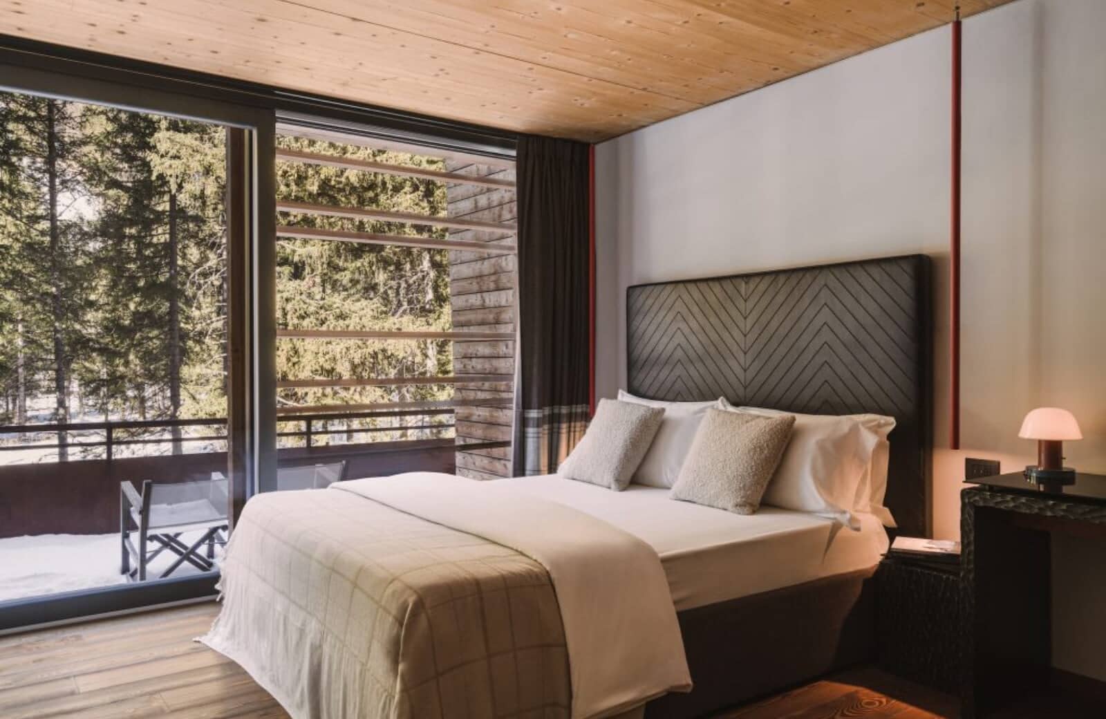 Bedroom with queen bed and floor-to-ceiling windows overlooking snowy woods