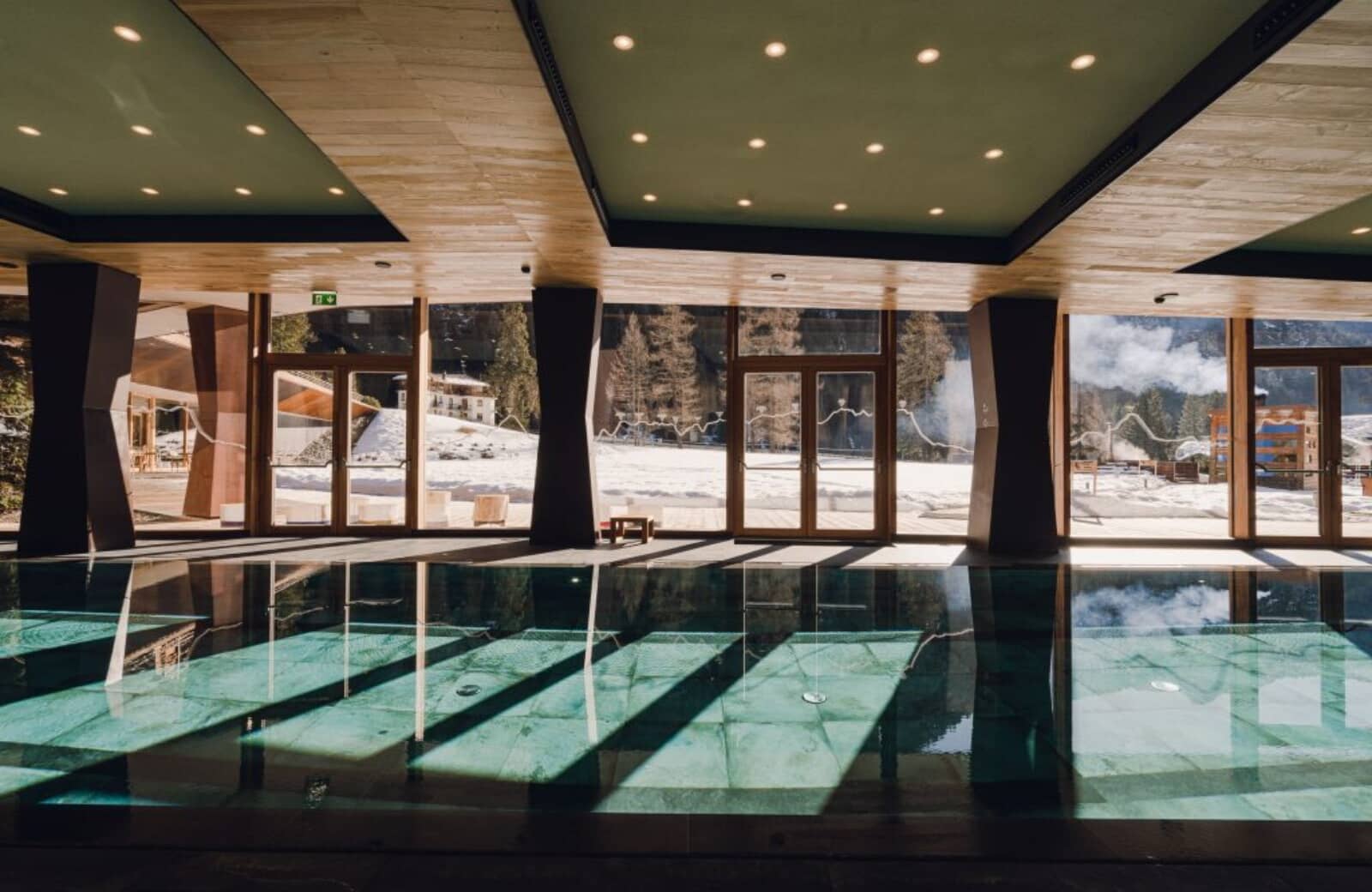 Indoor heated pool with floor-to-ceiling windows and snowy mountain views