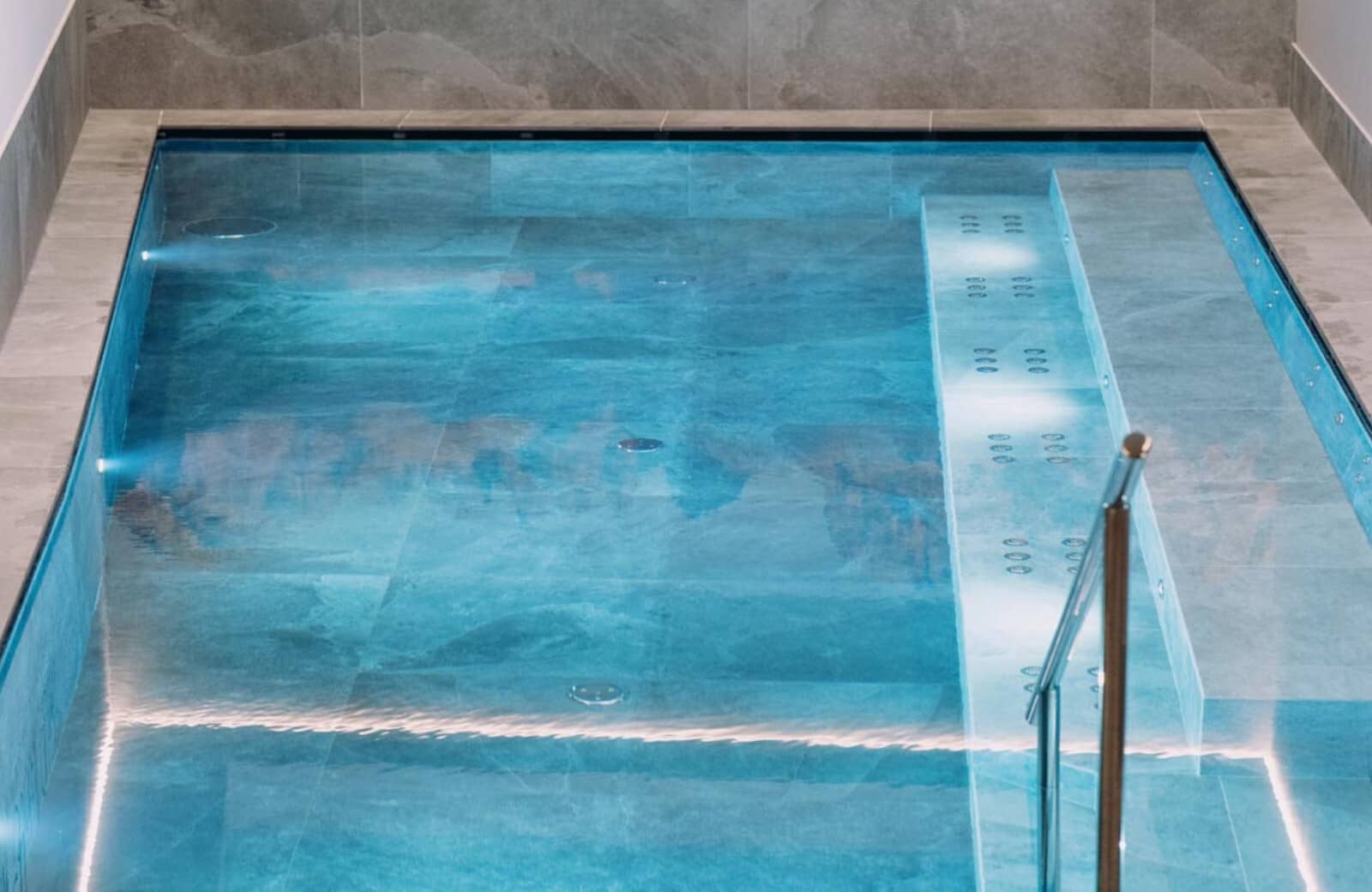 Indoor heated pool with handrail and submerged bench seating