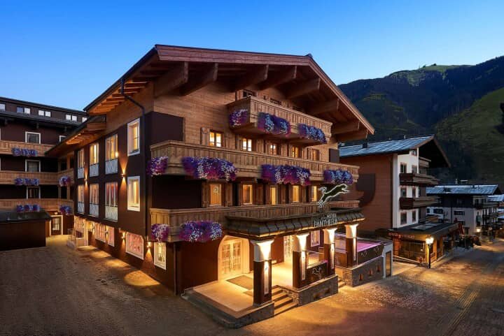 Alpine chalet exterior with purple petunias; illuminated evening entrance with multiple balconies