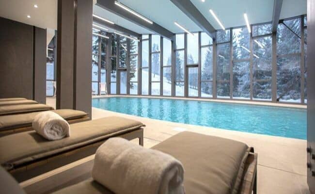 Indoor heated pool with floor-to-ceiling windows and snowy forest views