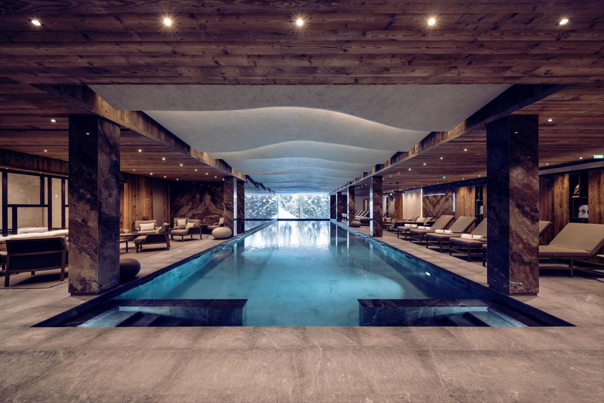Indoor heated lap pool with poolside loungers and forest view