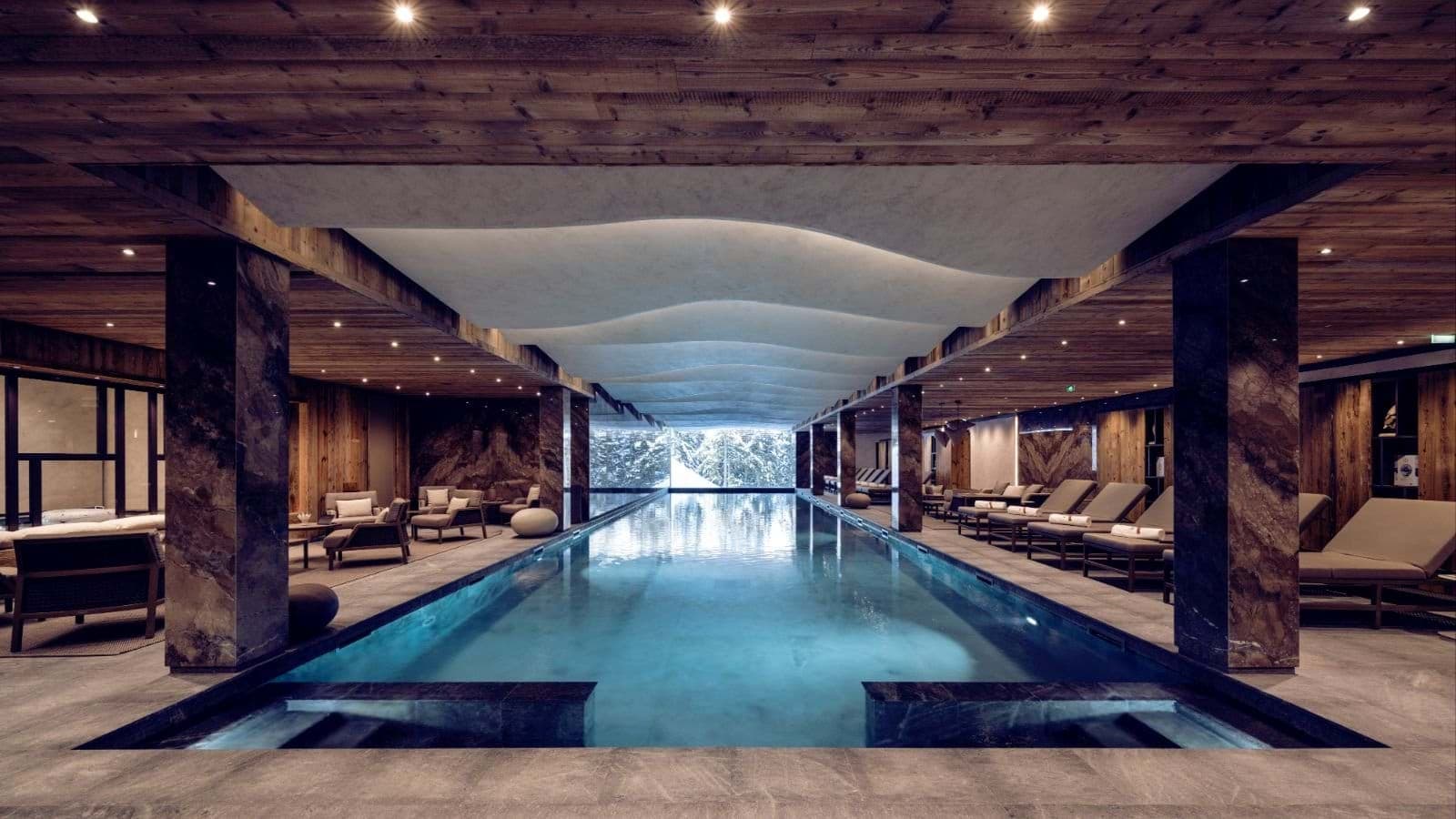 Indoor lap pool with poolside loungers and snowy forest views