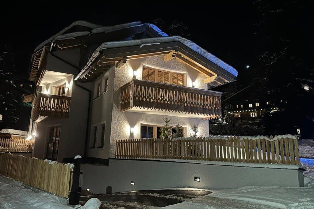 Chalet exterior at night with private driveway and upper-level balconies
