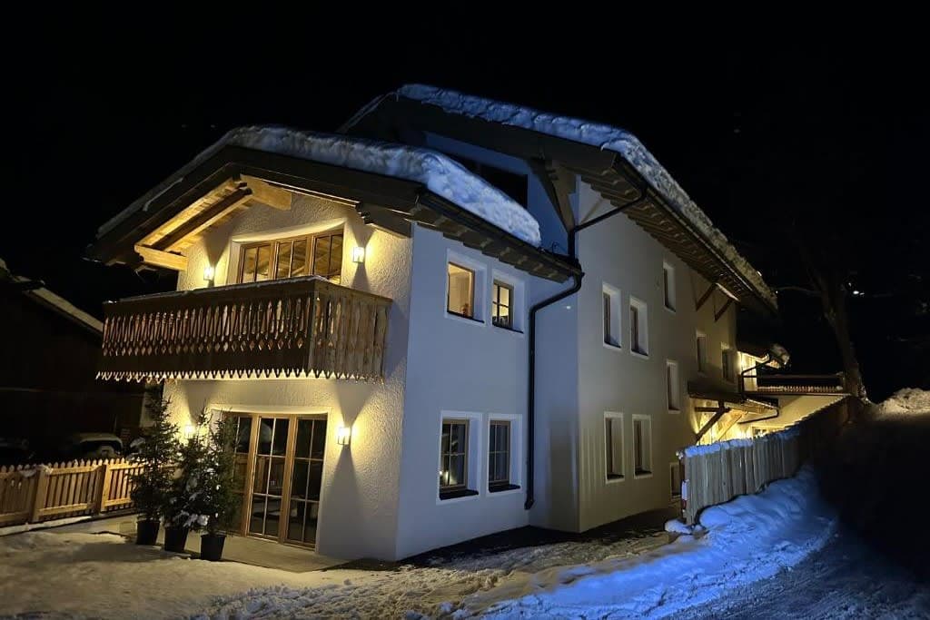 Chalet exterior at night with upper-level balcony and snowy grounds