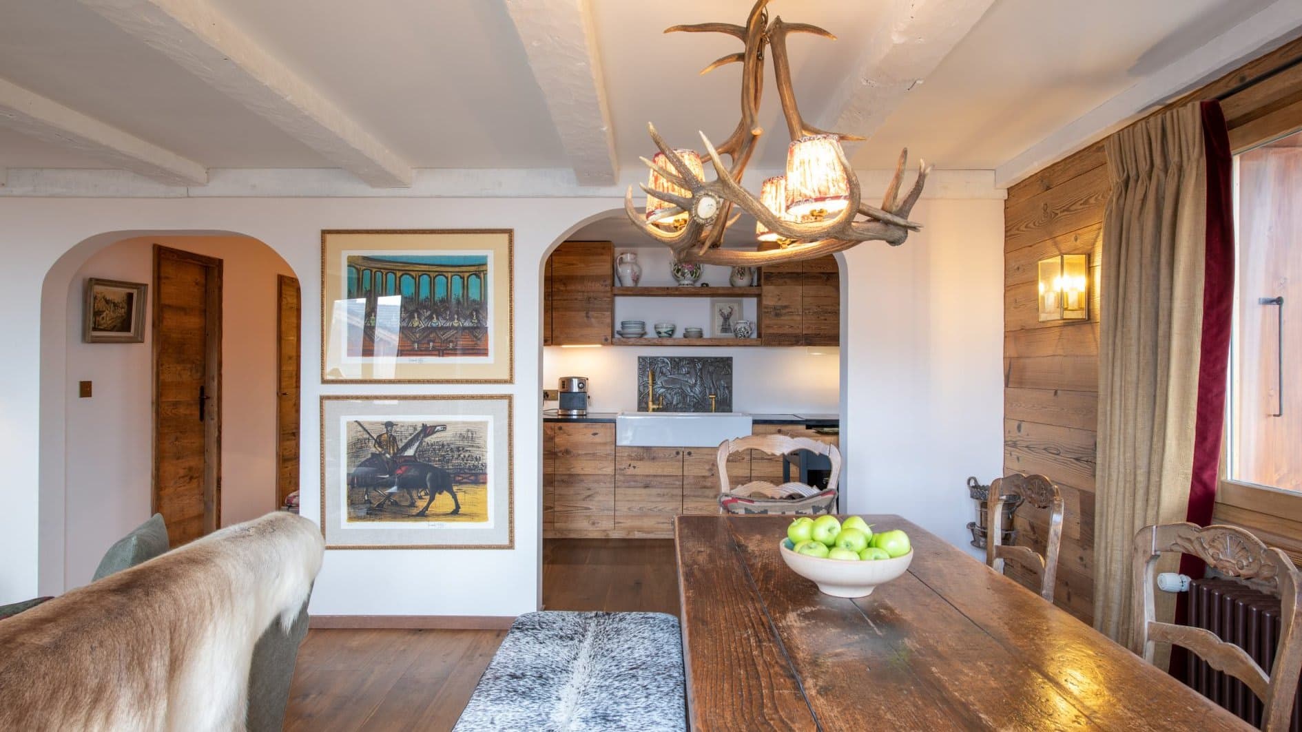 Dining area with antler chandelier; kitchen beyond arch features farmhouse sink