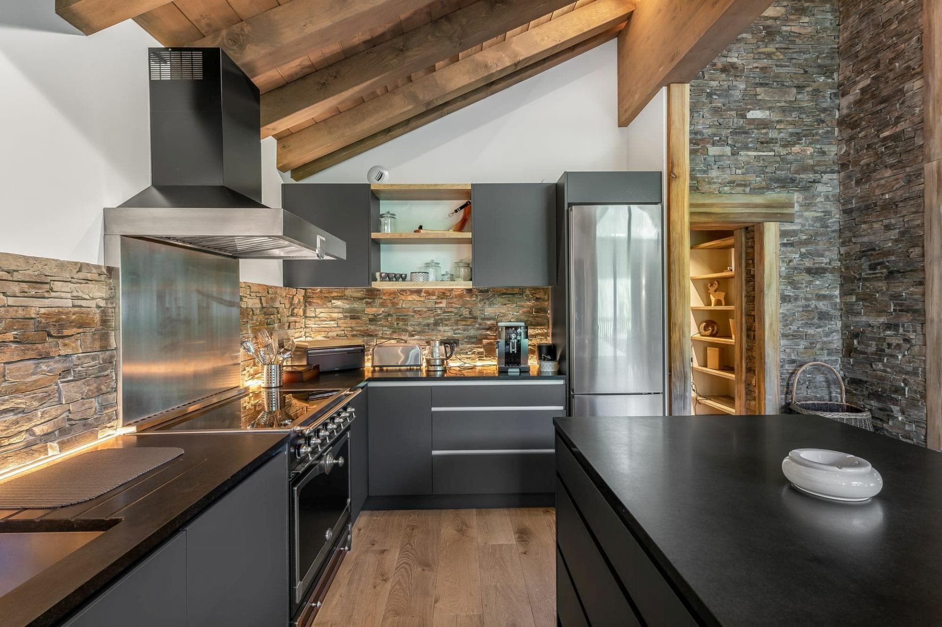 Open-plan fitted kitchen with stone worktops and mountain-style timber ceiling