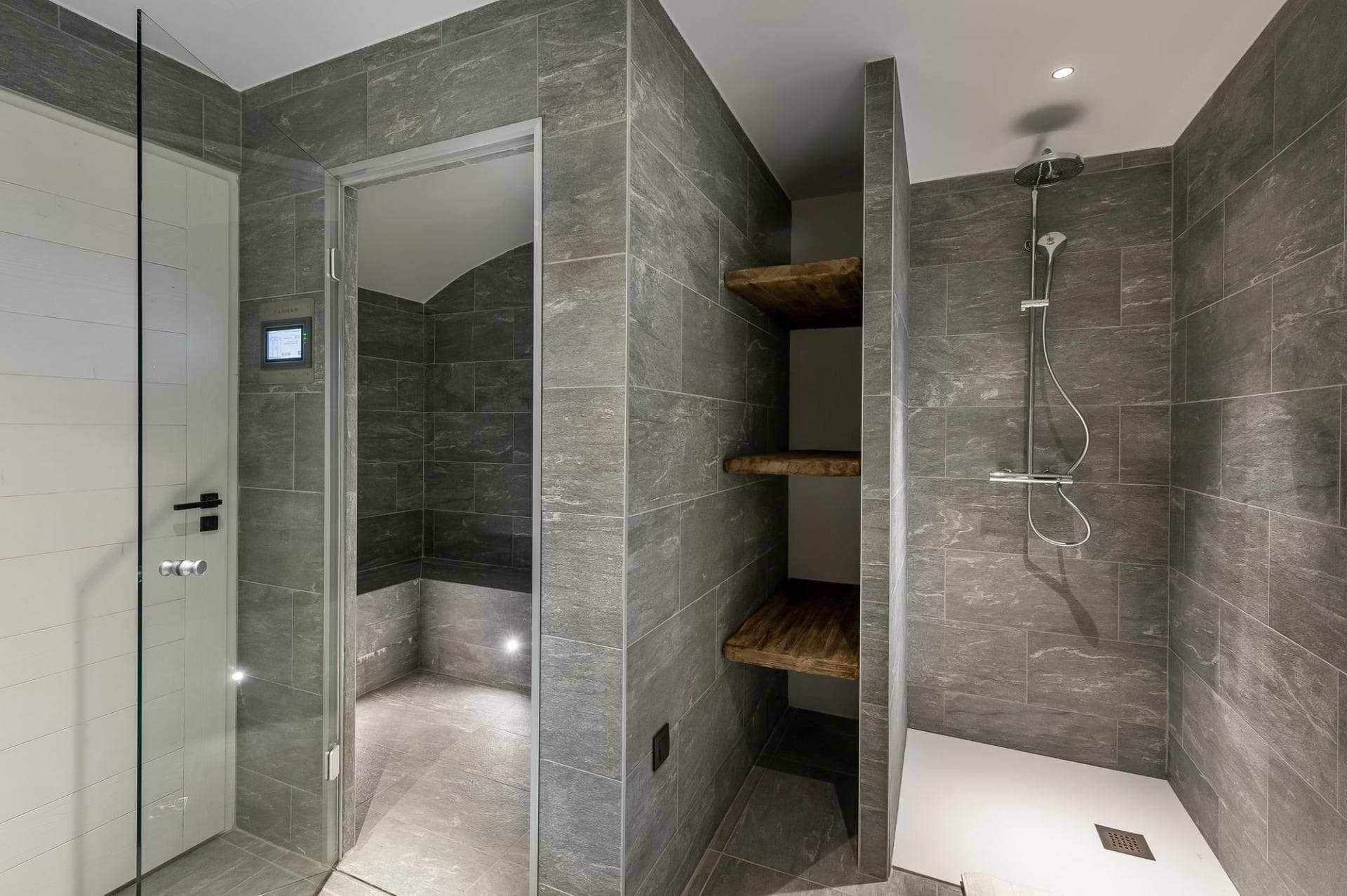 Walk-in rainfall shower adjacent to private steam room and wood shelving