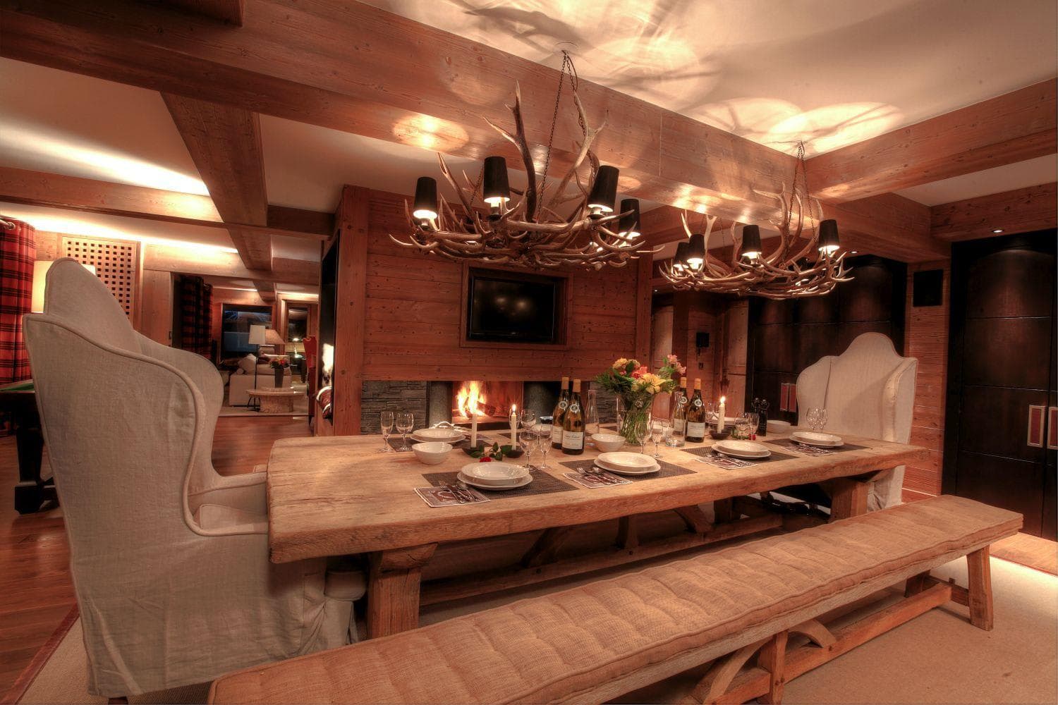 Dining area with wood-burning fireplace and antler chandeliers; bench and wingback seating