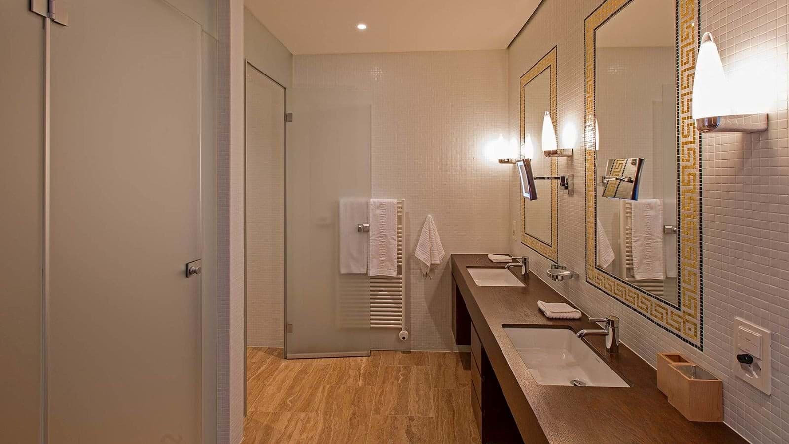 Bathroom with dual vanity, heated towel rack, and walk-in shower