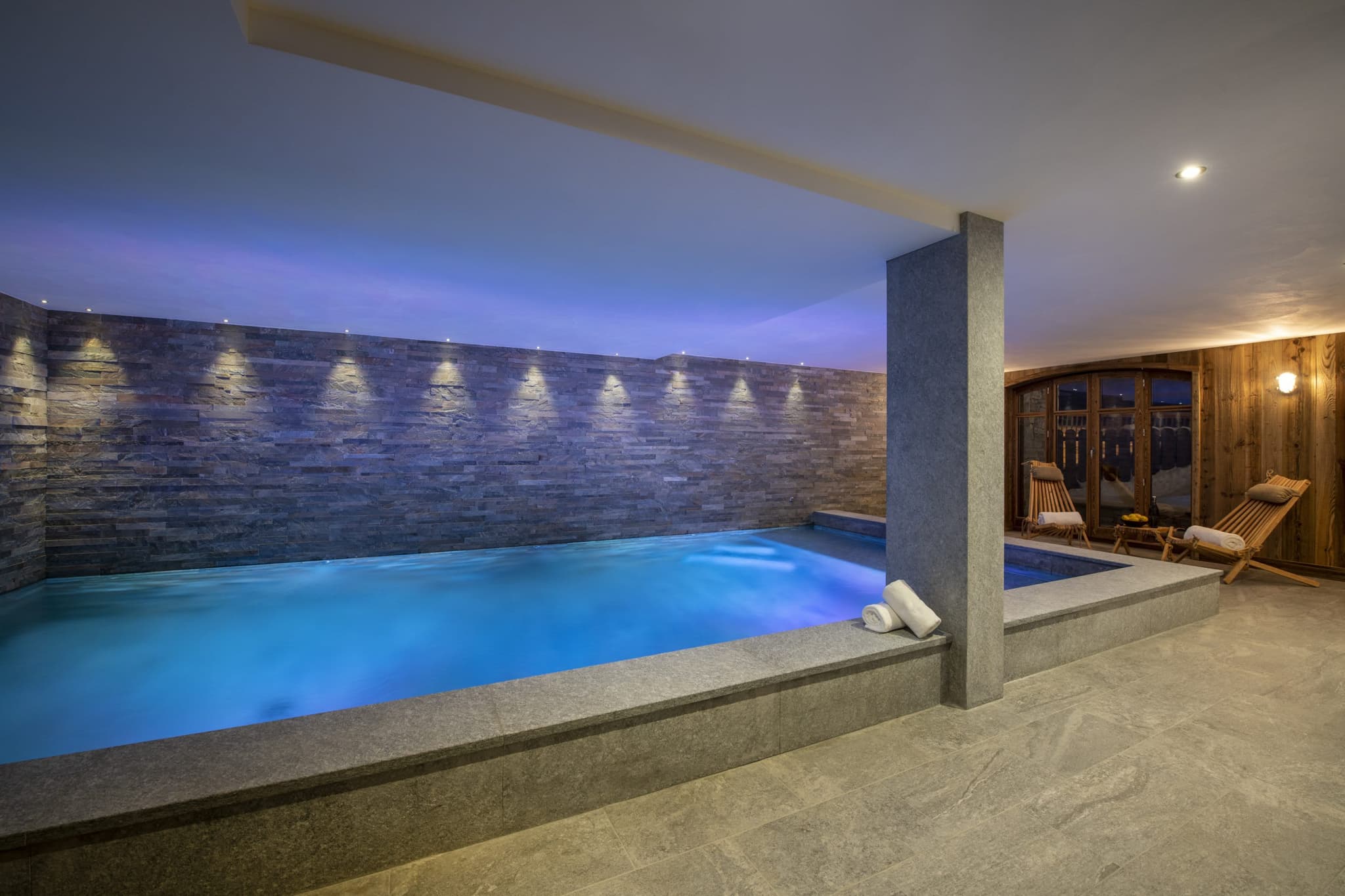 Indoor heated pool with stone feature wall and poolside lounge seating