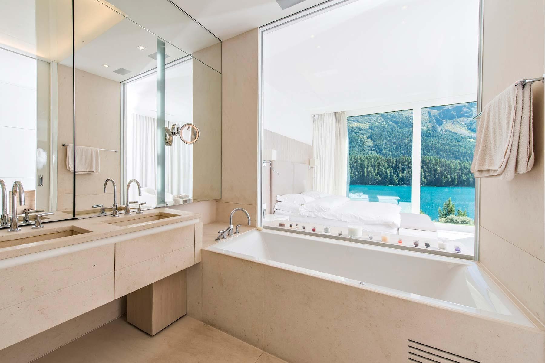 Primary bathroom with dual vanity and soaking tub; glass wall reveals lake views