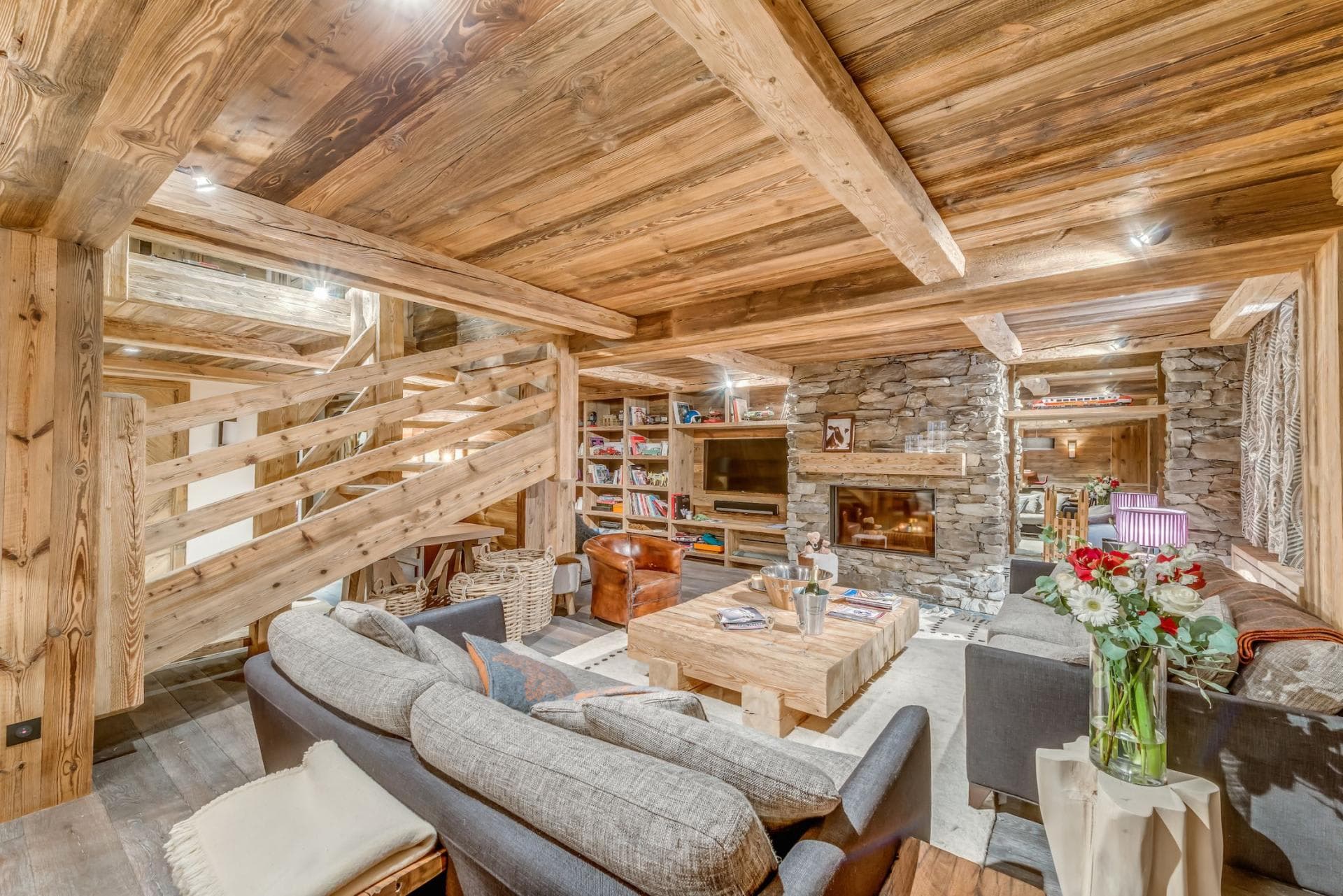 Living area with stone fireplace, timber beams, and built-in library