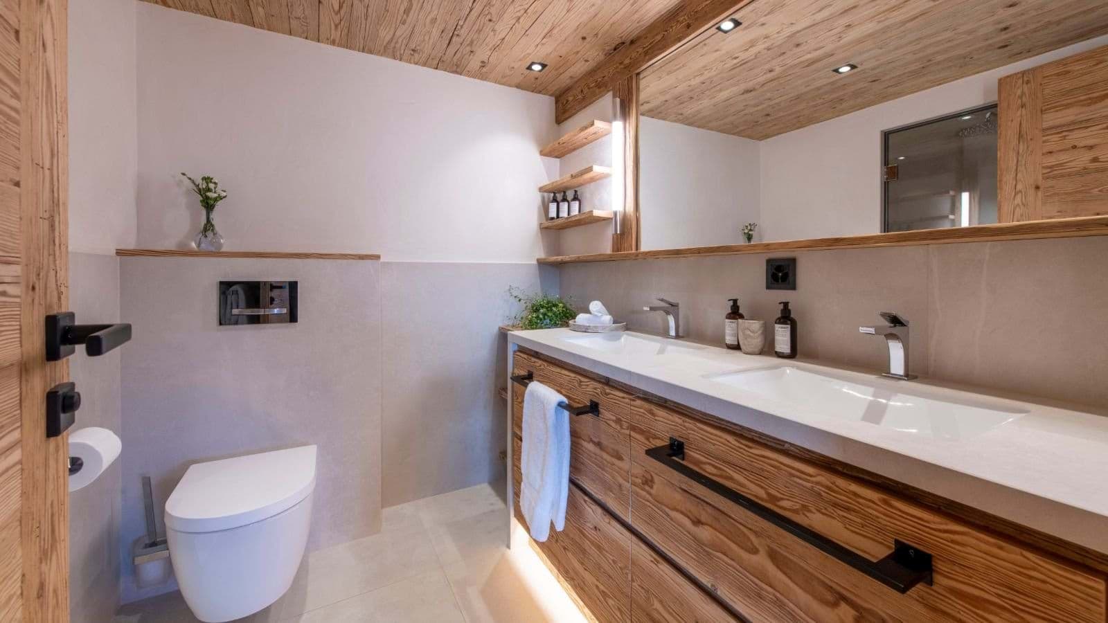 Bathroom with dual vanity, wood finishes, and wall-mounted toilet