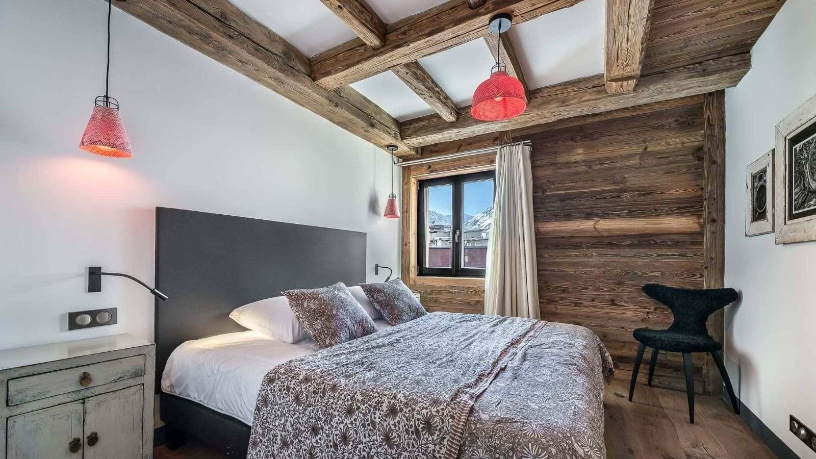 Bedroom with exposed beams, wood-clad walls, and mountain views through large window