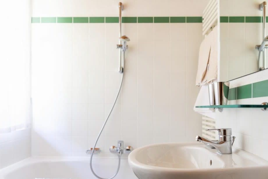 Bathroom with pedestal sink, heated towel rack, and bathtub shower