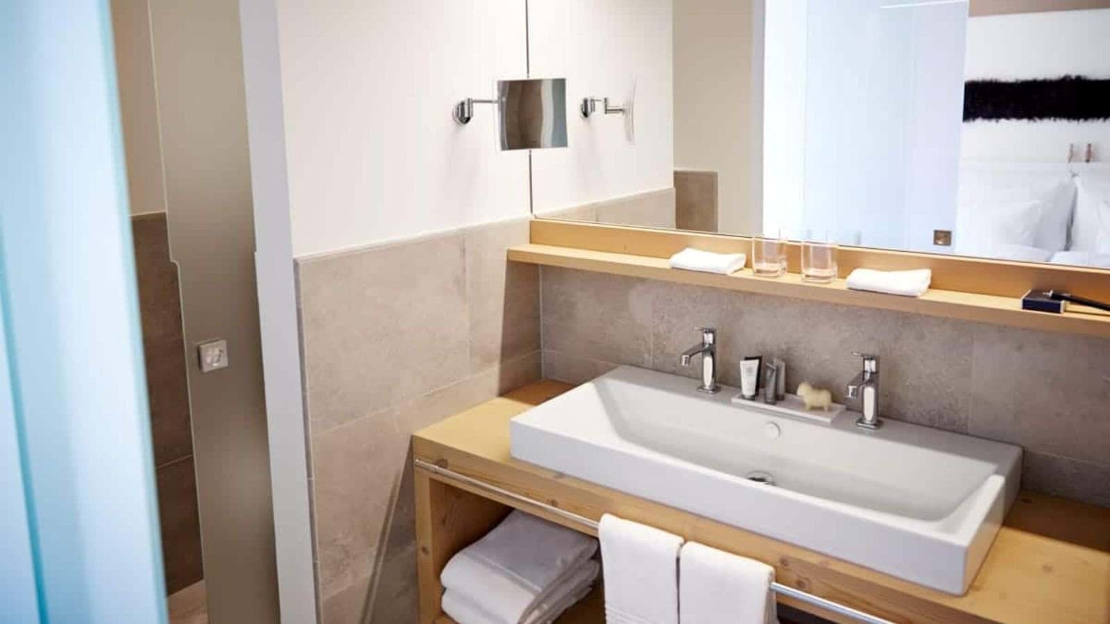 Bathroom with wide trough sink and wall-mounted magnifying mirror