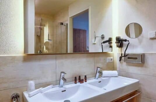 Bathroom with dual vanity, wall-mounted hairdryer, and backlit mirror