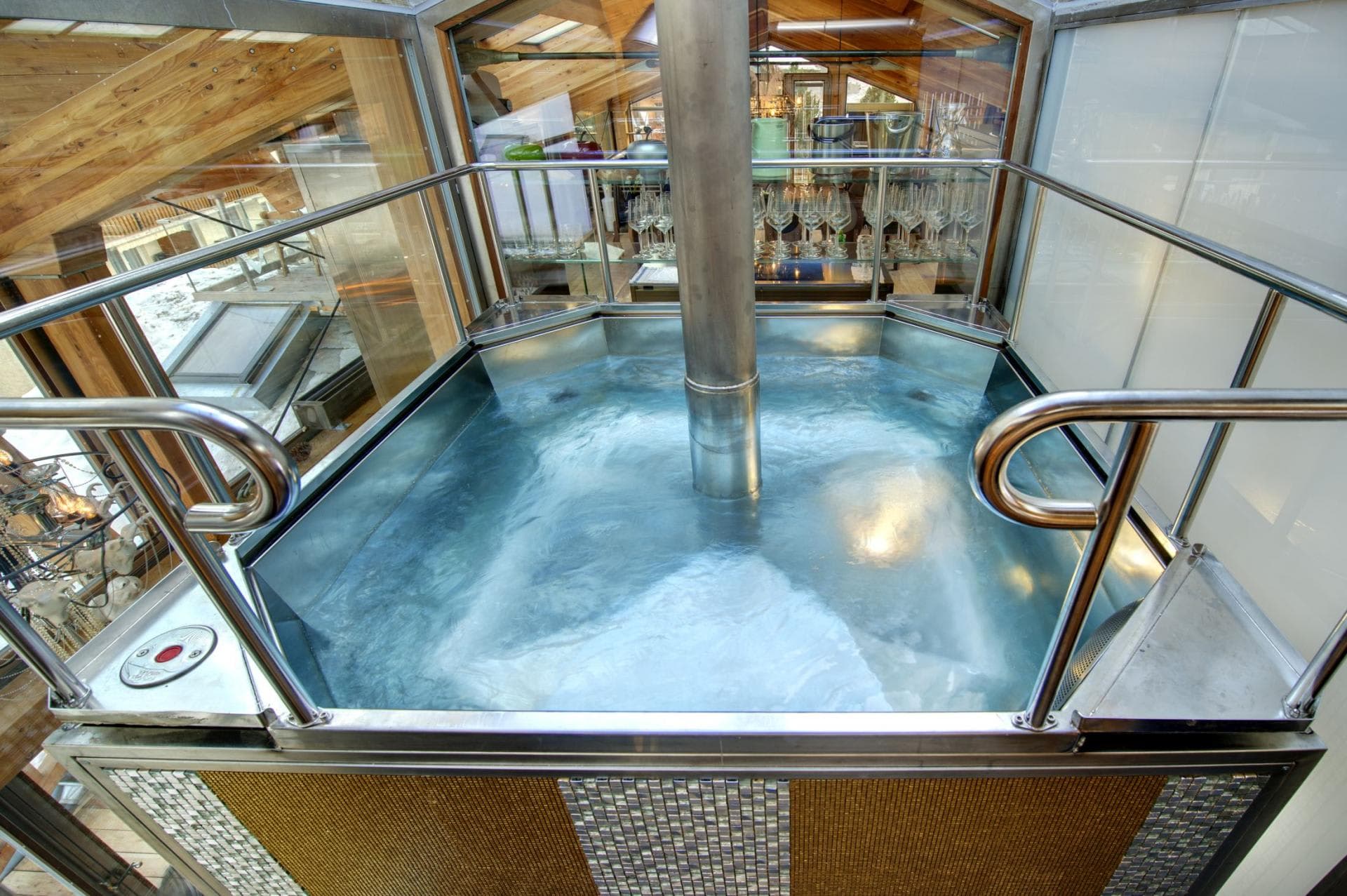 Indoor stainless steel hot tub with glass enclosure and wood-beamed ceilings