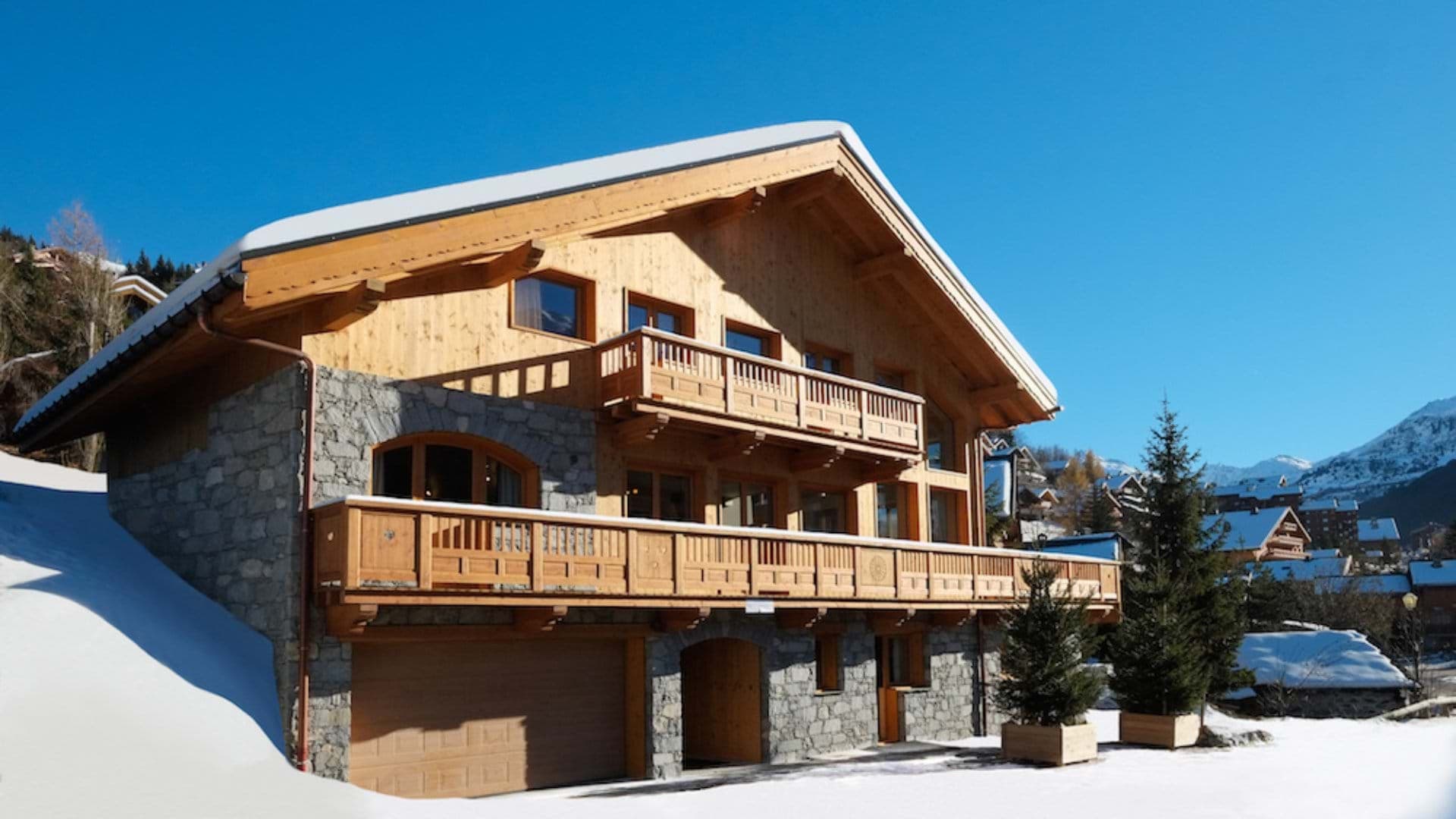 Ski-in chalet exterior featuring stone masonry, timber balconies, and integrated garage