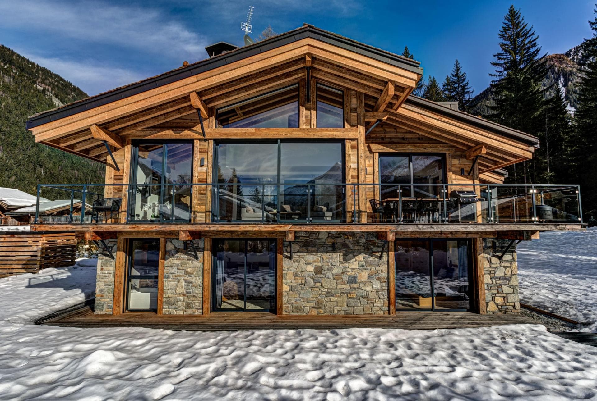 Chalet exterior with wrap-around balcony, gas grill, and stone facade