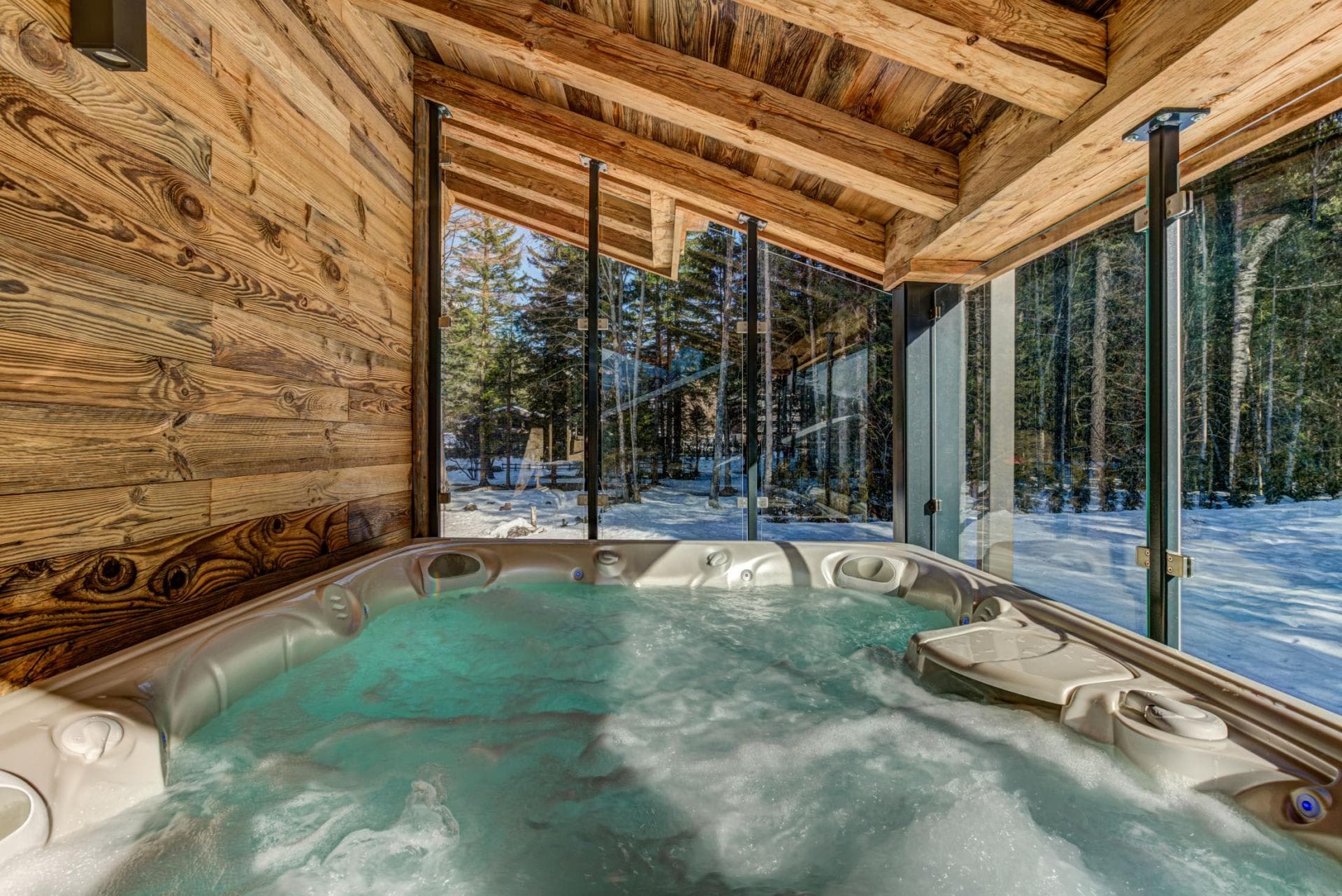 Covered outdoor hot tub with forest views and floor-to-ceiling glass enclosure