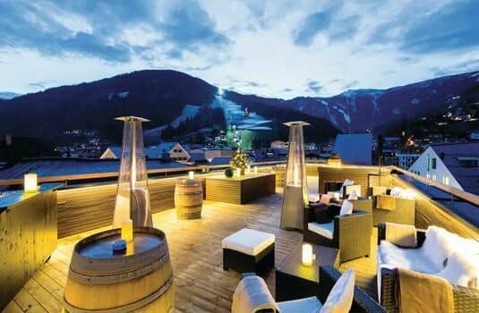 Rooftop lounge with heaters and views of illuminated ski slopes