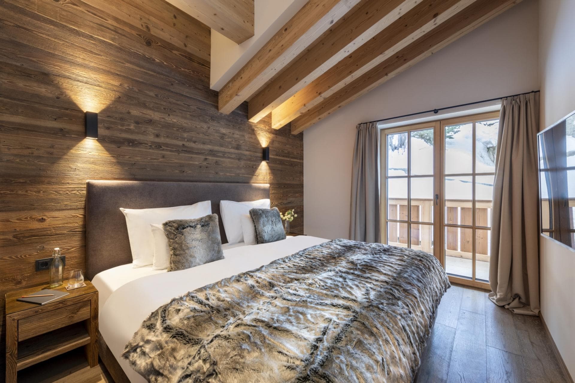 Primary bedroom with exposed beams, wood accent wall, and French doors to balcony