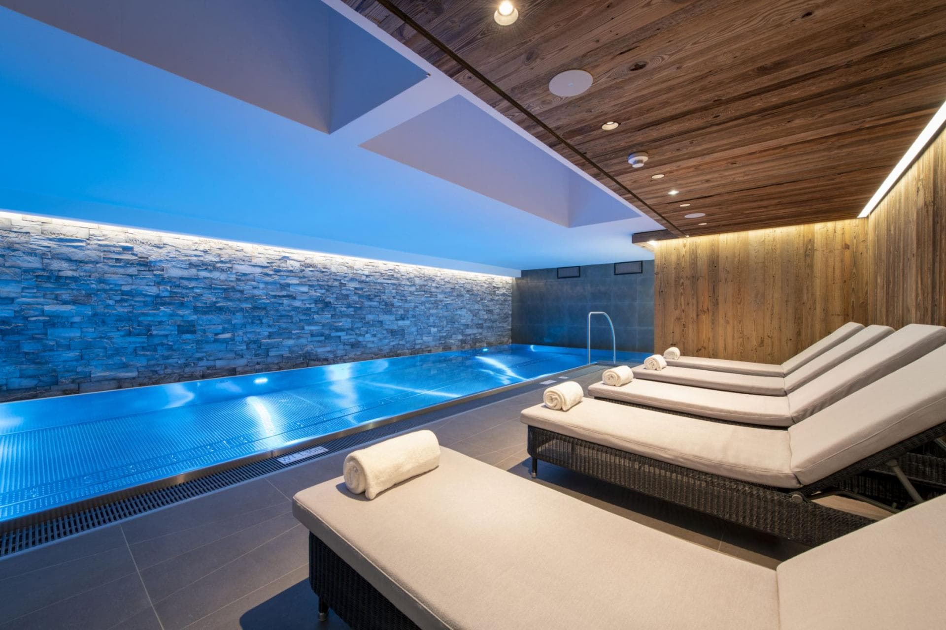 Indoor lap pool with five lounge chairs and stone feature wall