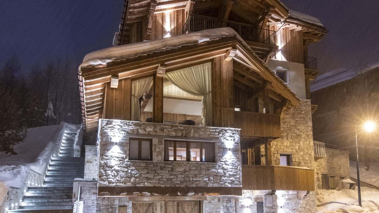 Chalet exterior at night with lit stairs and floor-to-ceiling windows