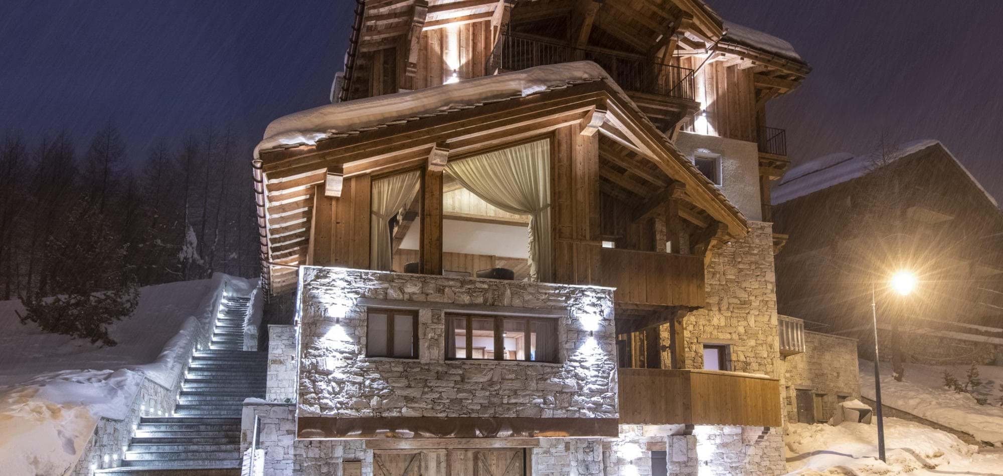 Chalet exterior at night with lit stone staircase and heated driveway access