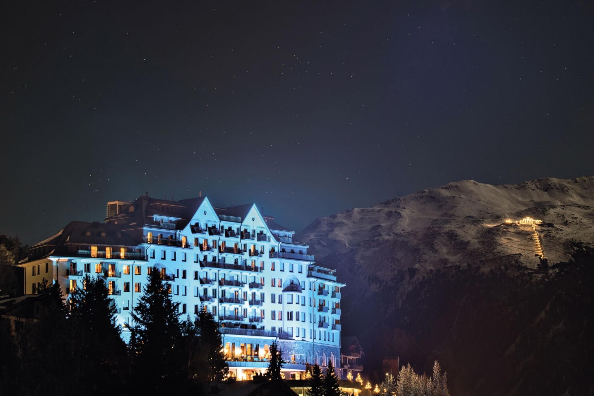 Lodge exterior at night; private balconies overlook lit mountain ski slopes