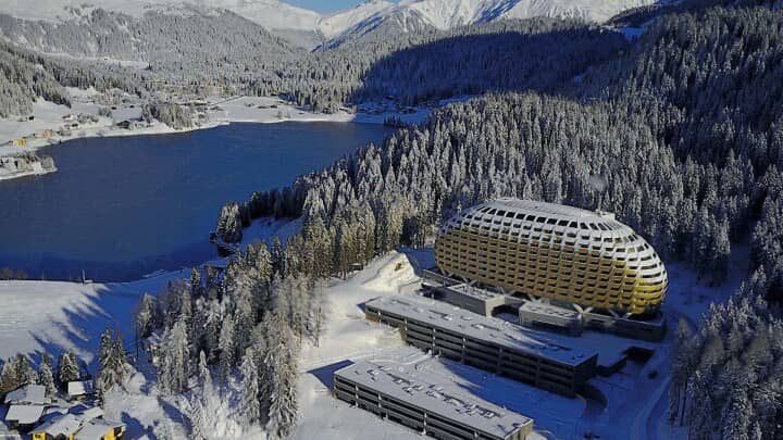 Aerial view of lakeside hotel with mountain and forest backdrop