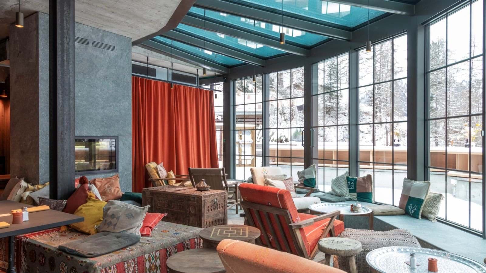 Sunroom lounge with glass ceiling and industrial steel frame overlooking snowy pines