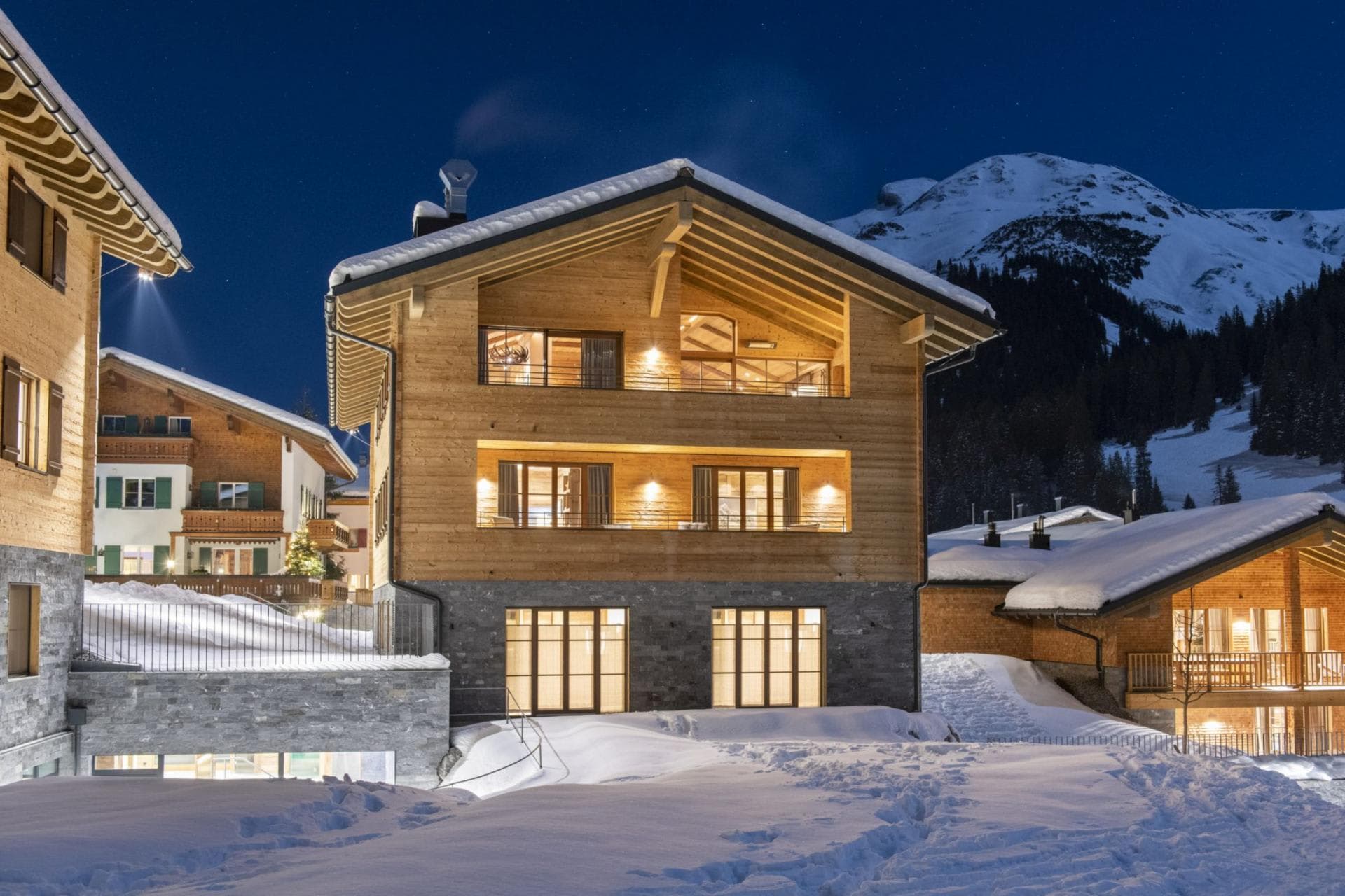 Chalet exterior with stone base and private balconies; snowy mountain backdrop