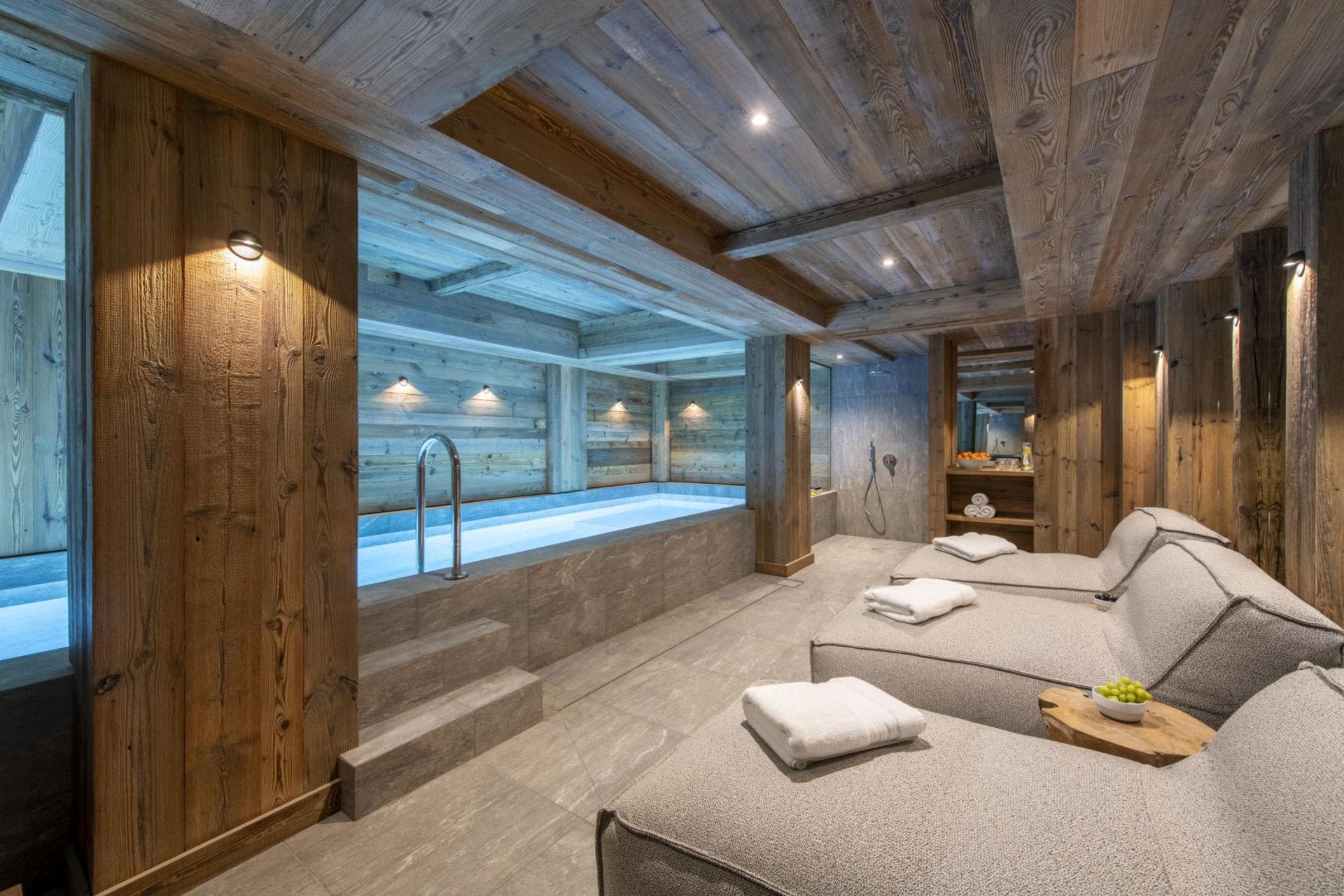 Indoor pool and spa area with three lounge chairs and rainfall shower