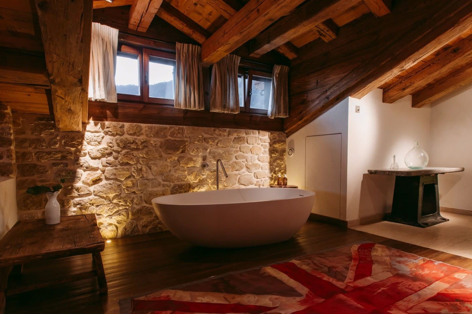 Bathroom with freestanding soaking tub, exposed stone wall, and timber beams