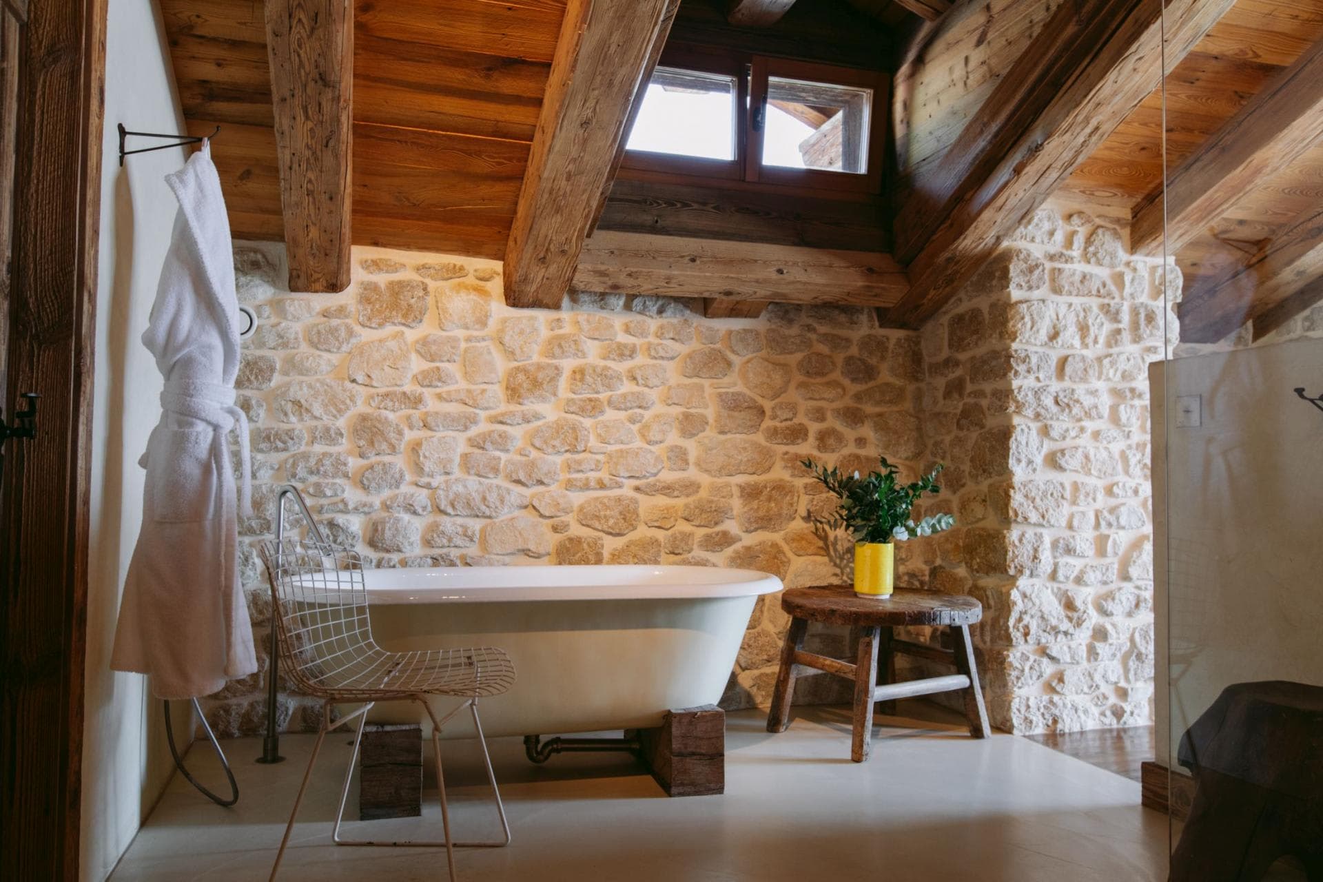 Bathroom with freestanding tub, exposed stone walls, and timber ceiling beams
