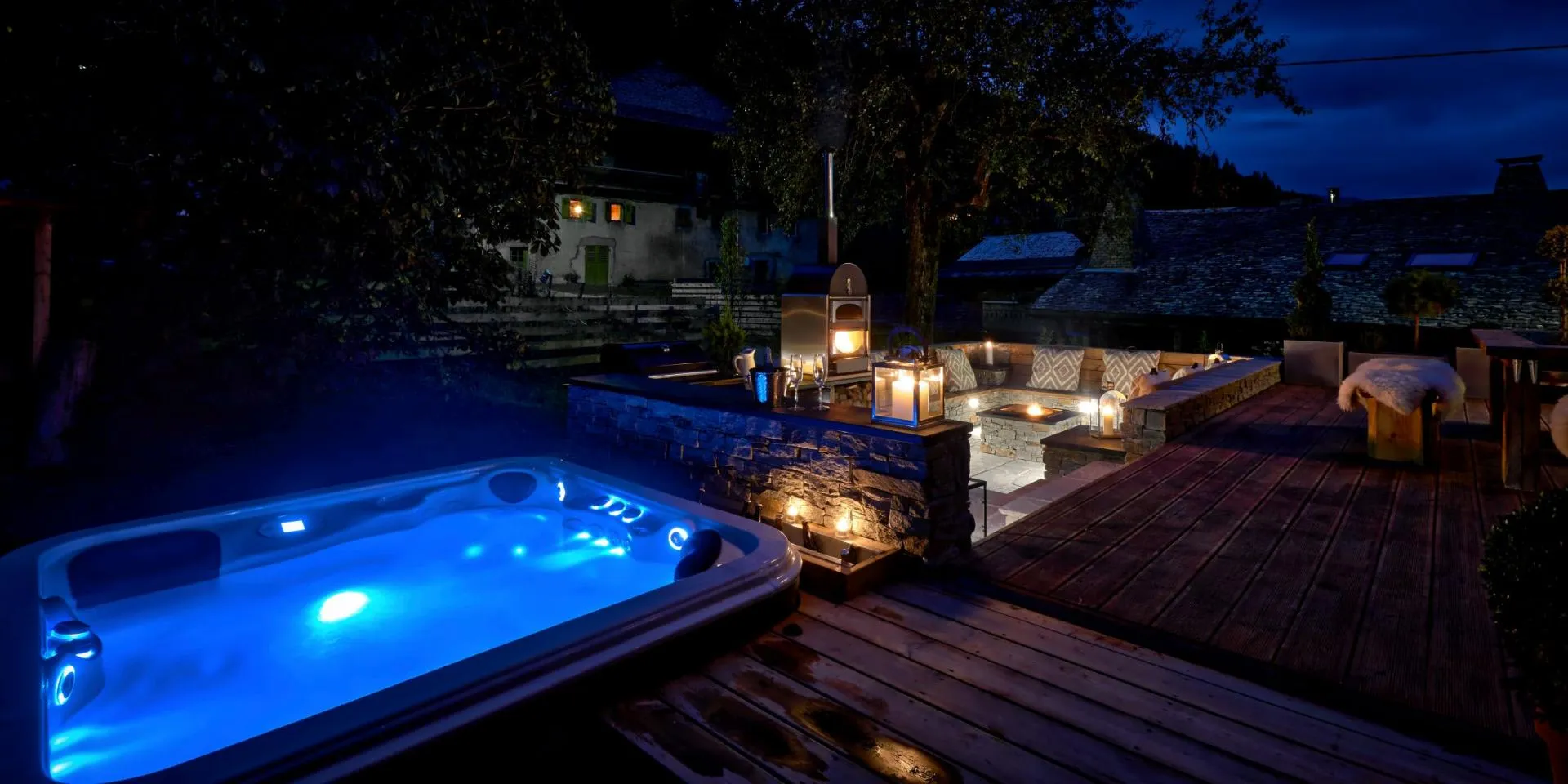 Outdoor terrace with illuminated hot tub, pizza oven, and sunken fire pit