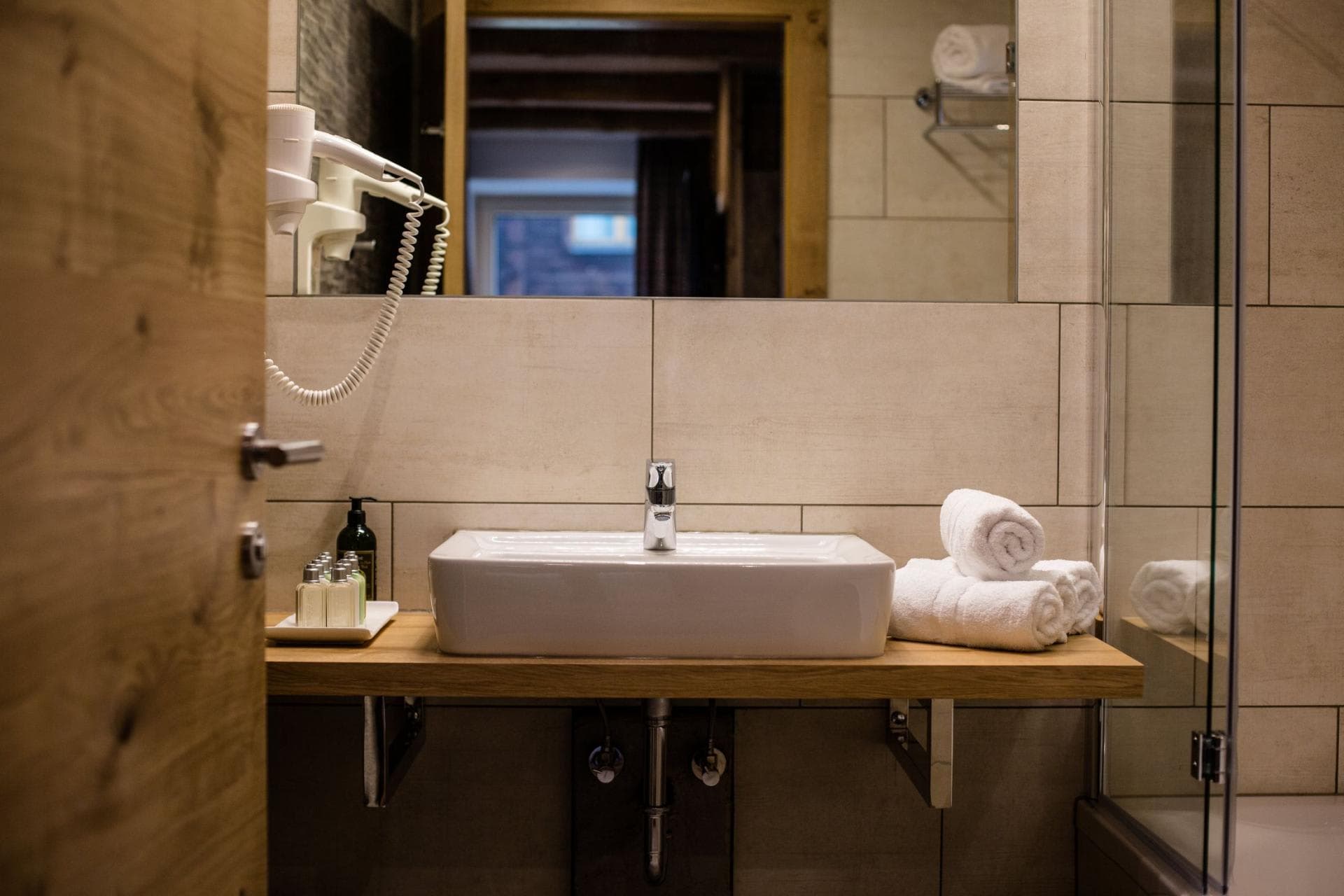 Bathroom vanity with vessel sink, wall-mounted hairdryer, and toiletries