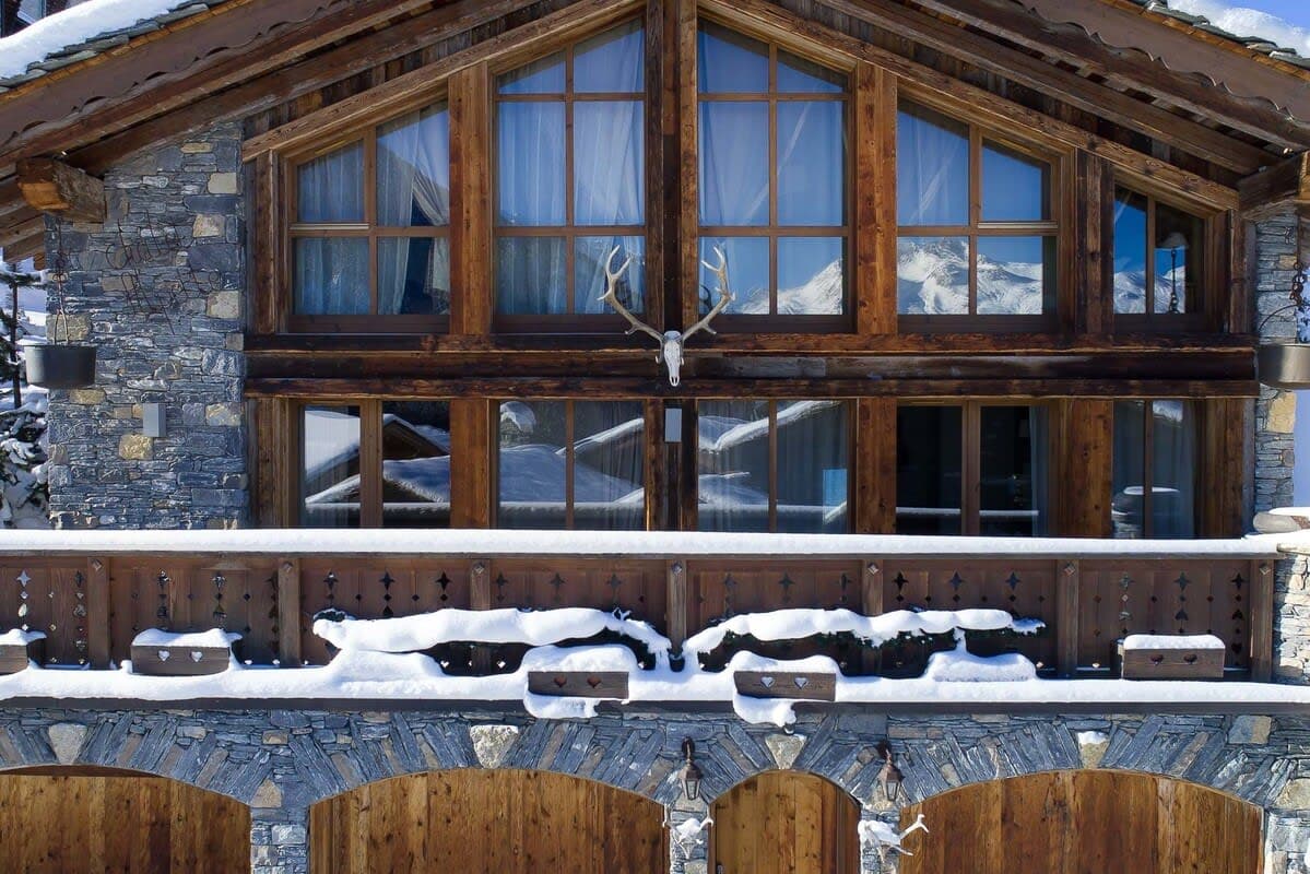 Chalet exterior with stone masonry and private balcony overlooking snow-capped mountains