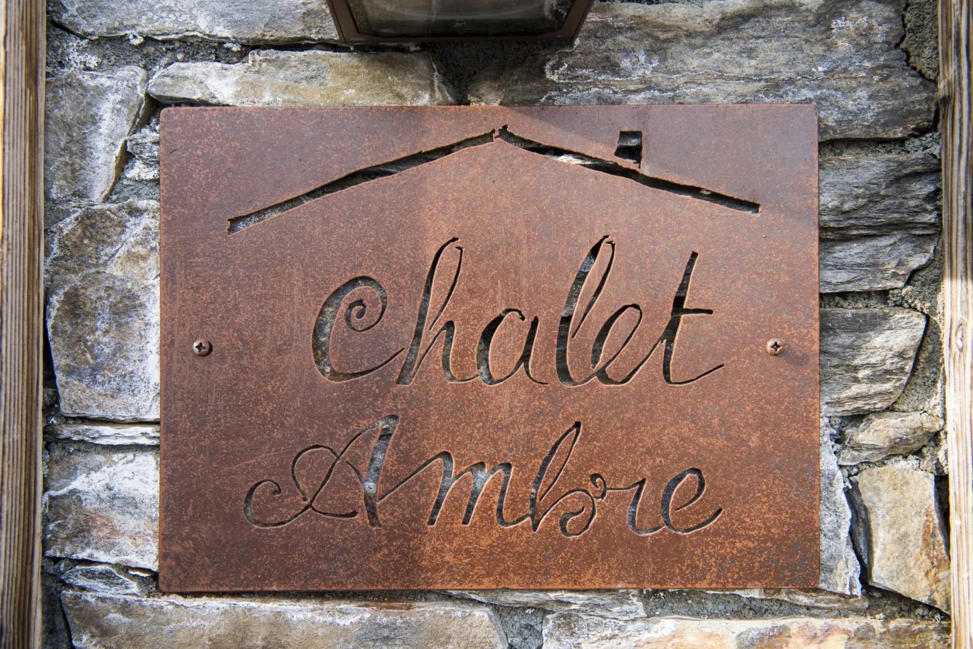 Custom steel entrance sign for Chalet Ambre on natural stone facade