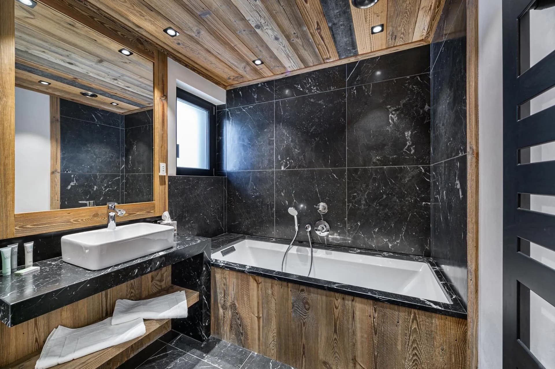 Bathroom with a bath, vanity and dark stone tiles