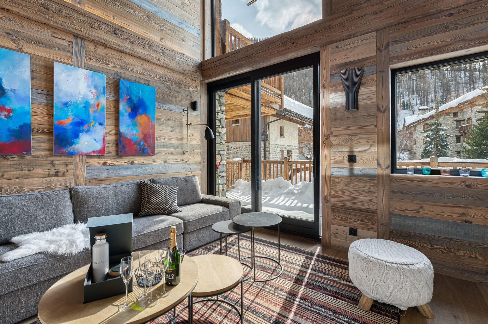 Living area with wood-paneled walls and balcony access overlooking the village