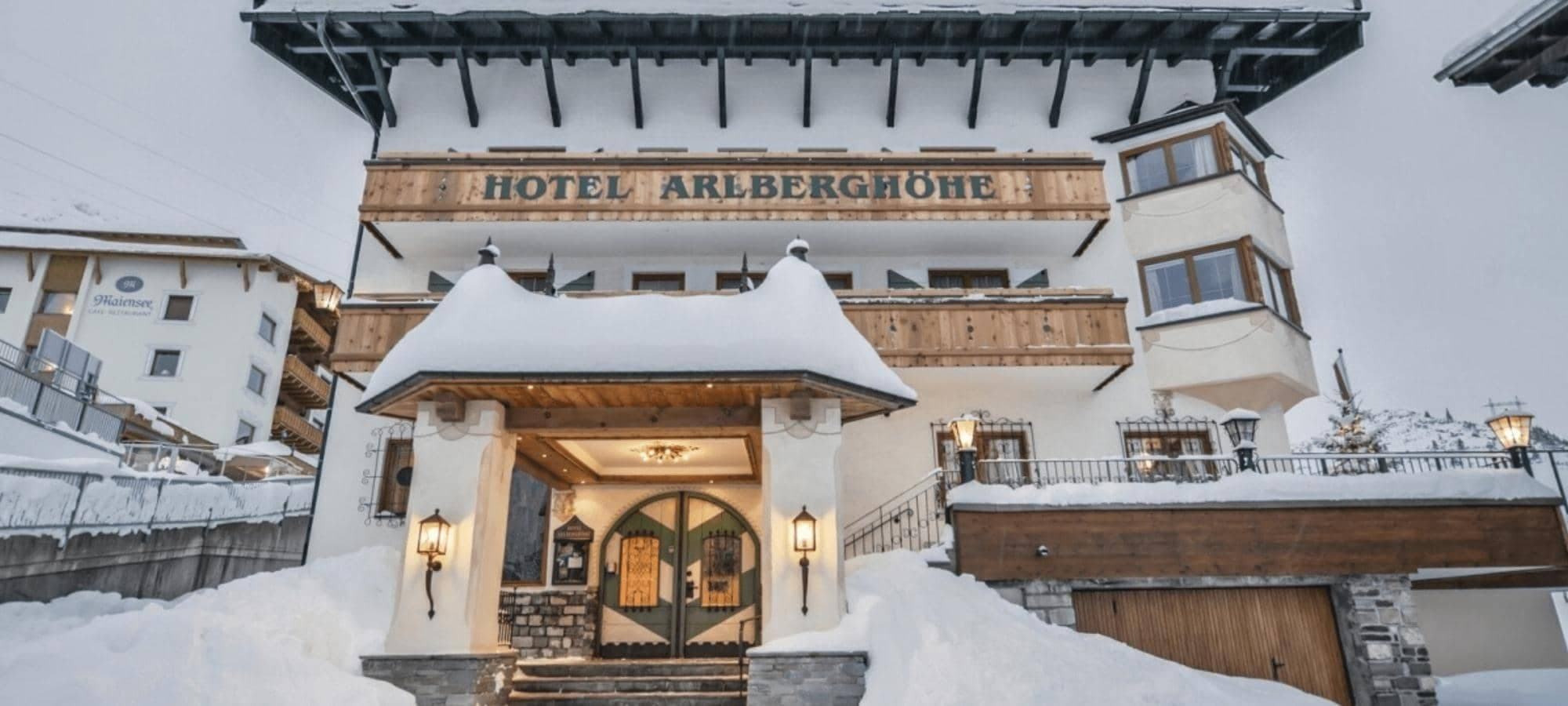 Hotel Arlberghöhe exterior featuring wooden balconies and snow-covered entrance