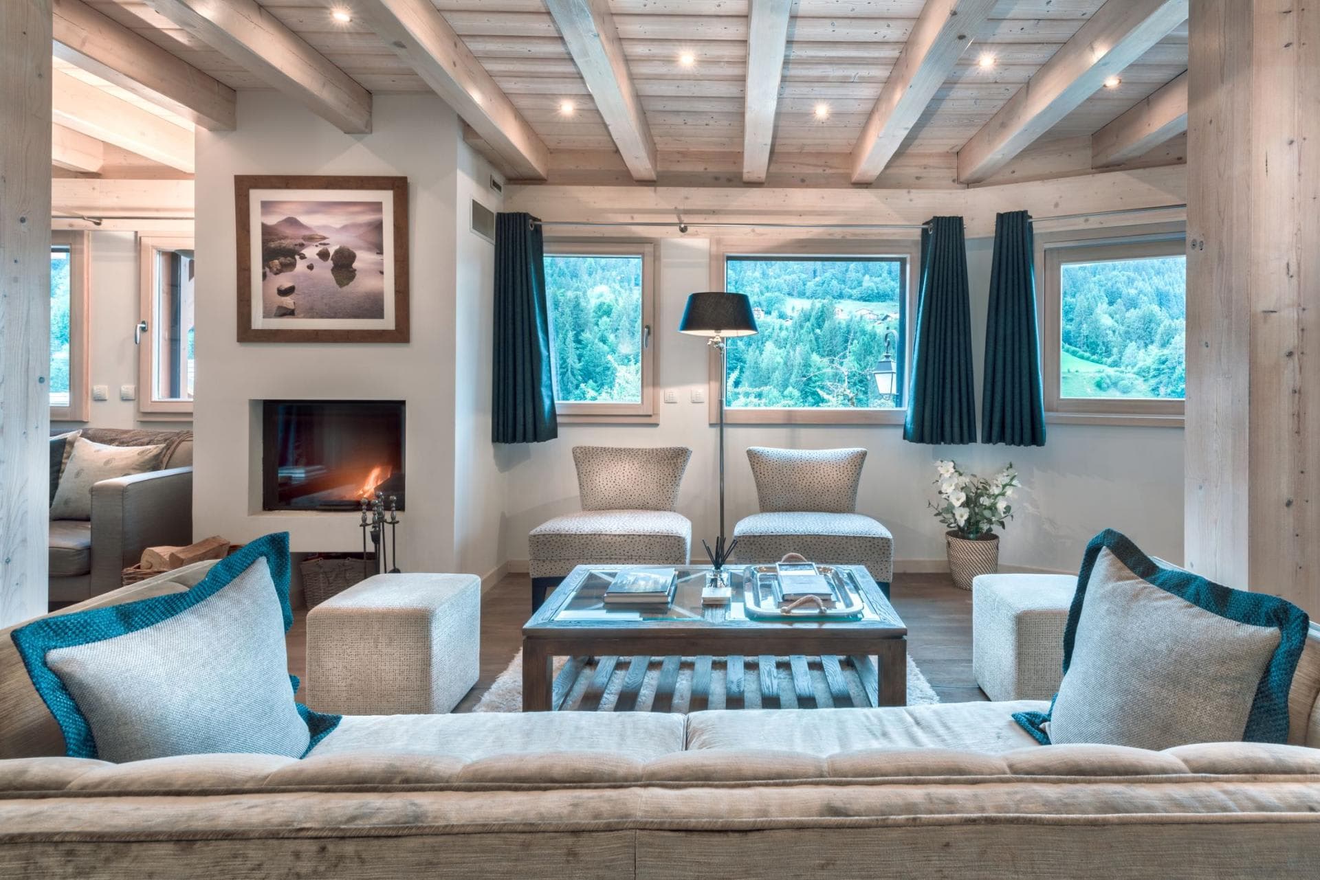 Living area with wood-beam ceiling, wood-burning fireplace, and alpine forest views