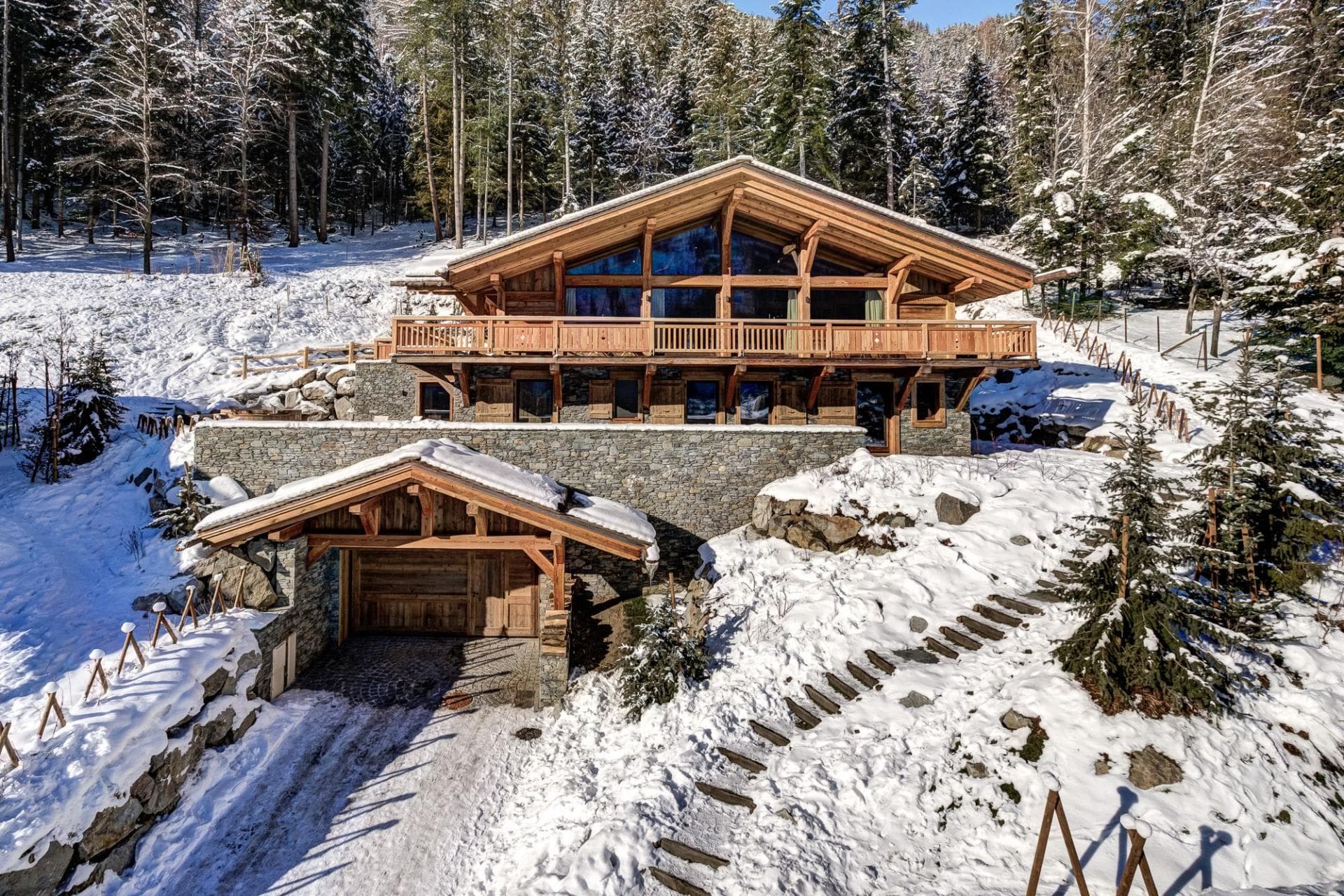 Timber chalet with stone base, garage, and balcony overlooking pine forest